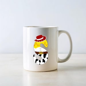 Peut inclure: Mug en c&eacute;ramique blanche avec la lettre "S" d&eacute;cor&eacute;e sur le th&egrave;me du cowboy. La lettre pr&eacute;sente un chapeau rouge, une chemise jaune, une ceinture marron et un motif de vache, pour un style amusant et cartoon.