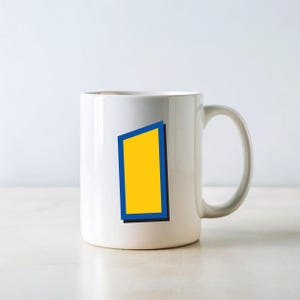 Peut inclure: Mug en c&eacute;ramique blanche avec un rectangle jaune bord&eacute; de bleu et une ombre noire. La tasse a une anse incurv&eacute;e et est pos&eacute;e sur un fond blanc. Le design est simple et moderne.