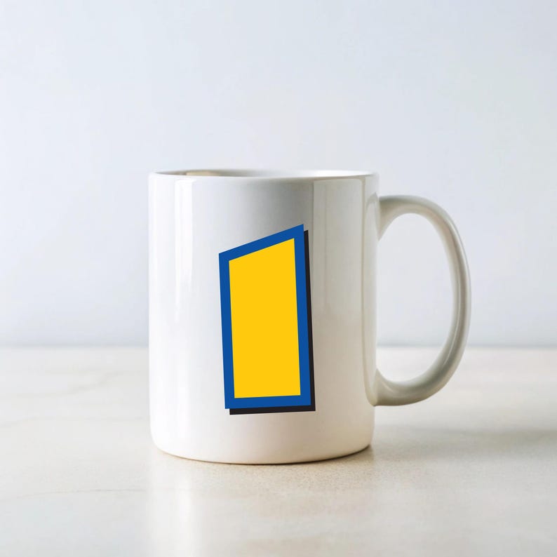 Peut inclure: Mug en c&eacute;ramique blanche avec un rectangle jaune bord&eacute; de bleu et une ombre noire. La tasse a une anse incurv&eacute;e et est pos&eacute;e sur un fond blanc. Le design est simple et moderne.