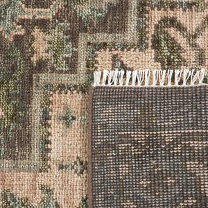 May include: A woven rug featuring a dark brown and light pink floral pattern with sage green accents. The rug has a visible textured pile and a white fringe along the edge, showing both the detailed top surface and the dark brown woven backing.