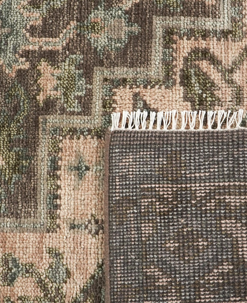 May include: A woven rug featuring a dark brown and light pink floral pattern with sage green accents. The rug has a visible textured pile and a white fringe along the edge, showing both the detailed top surface and the dark brown woven backing.