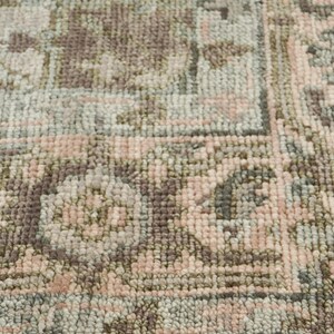 May include: Close-up of a rectangular rug with a detailed, faded floral pattern. The rug features a color palette of muted pink, sage green, and brown tones. The design includes a border and a central pattern.