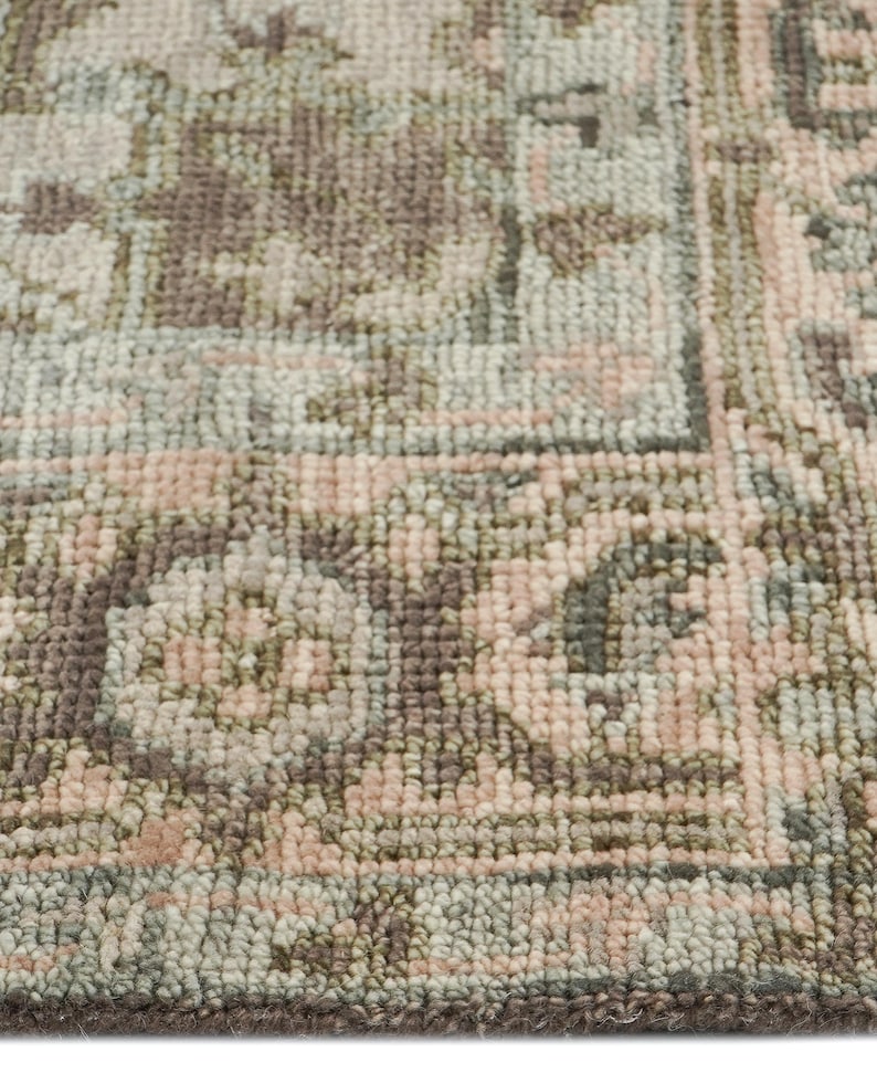 May include: Close-up of a rectangular rug with a detailed, faded floral pattern. The rug features a color palette of muted pink, sage green, and brown tones. The design includes a border and a central pattern.