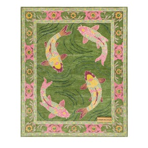 Op de afbeelding: Een rechthoekig vloerkleed met een groene achtergrond en drie koikarpers in roze, gele en paarse tinten. Het kleed heeft een decoratieve rand met roze en gele bloemmotieven. Een klein rechthoekig label bevat de tekst HANKWOVEN.