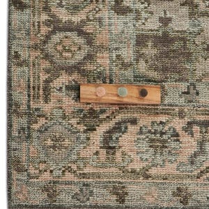 May include: Close-up of a patterned rug with a distressed, vintage look. The rug features a mix of muted colors, including green, brown, and pink. A small wooden swatch board with three color samples sits on top of the rug, showcasing the color palette.