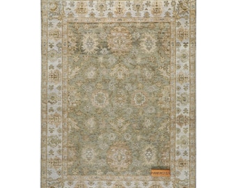 May include: Rectangular area rug with a central sage green field and an ornate border in cream and tan. The rug features a detailed floral pattern and a rectangular label that reads "HANKWOVEN".