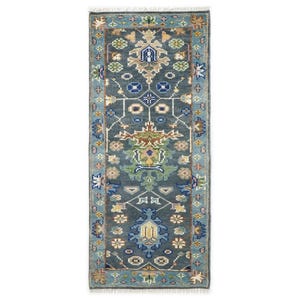 Op de afbeelding: Een rechthoekig vloerkleed met een patroon in blauw- en turkooistinten. Het vloerkleed heeft een centraal ontwerp met bloemen en geometrische motieven in beige, groen en geel. De rand is licht turquoise met vergelijkbare bloempatronen.