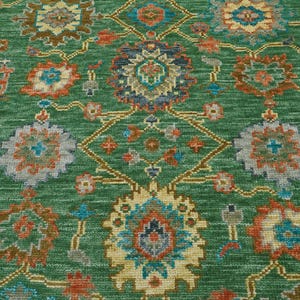 Op de afbeelding: Groen vloerkleed met een ingewikkeld bloemenpatroon. Het kleed heeft een centraal medaillonontwerp en een herhalend patroon van bloemen in tinten oranje, blauw en cr&egrave;me. De achtergrond is effen groen en het kleed heeft een getextureerde uitstraling.