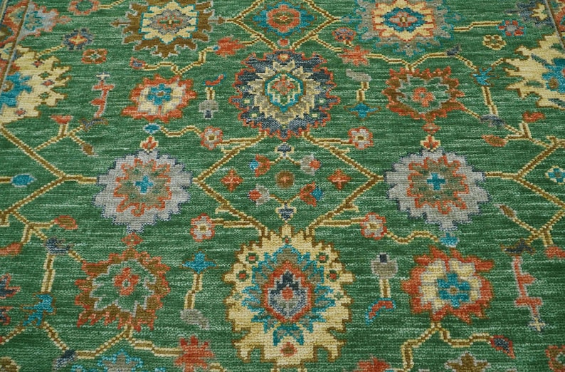 Op de afbeelding: Groen vloerkleed met een ingewikkeld bloemenpatroon. Het kleed heeft een centraal medaillonontwerp en een herhalend patroon van bloemen in tinten oranje, blauw en cr&egrave;me. De achtergrond is effen groen en het kleed heeft een getextureerde uitstraling.