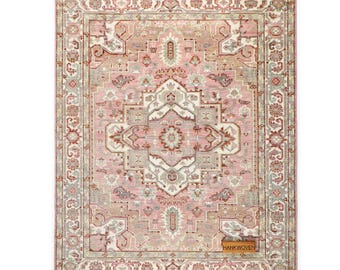 May include: A rectangular, hand-woven rug with a central medallion design. The rug features a soft pink background with intricate patterns in shades of gray, brown, and cream. The border is detailed with floral motifs. The tag reads "HANKWOVEN".