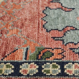 Puede incluir: Primer plano de una secci&oacute;n de una alfombra con un patr&oacute;n detallado e intrincado. La alfombra presenta una paleta de colores coral, naranja, verde y azul. El borde es azul marino oscuro con motivos florales.