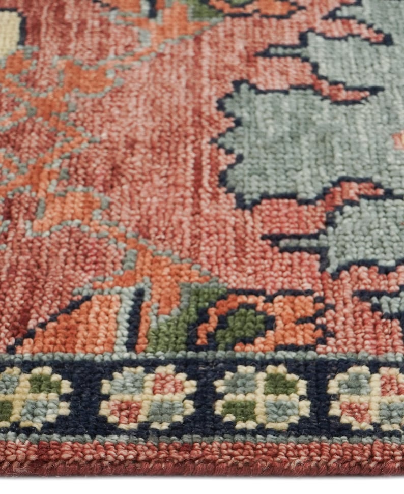 Puede incluir: Primer plano de una secci&oacute;n de una alfombra con un patr&oacute;n detallado e intrincado. La alfombra presenta una paleta de colores coral, naranja, verde y azul. El borde es azul marino oscuro con motivos florales.