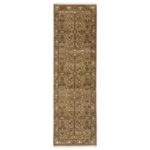 Puede incluir: Una alfombra rectangular estrecha de color beige con un intrincado diseño floral en tonos marrones y crema. La alfombra tiene un borde con flecos y un diseño simétrico.