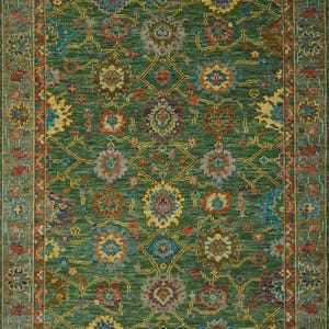 Op de afbeelding: Een rechthoekig groen tapijt met een ingewikkeld bloemmotief in tinten blauw, geel, rood en bruin. Het tapijt heeft een gedetailleerde rand met vergelijkbare kleuren en ontwerpen. Het algehele ontwerp is symmetrisch en sierlijk, voor interieurdecoratie.