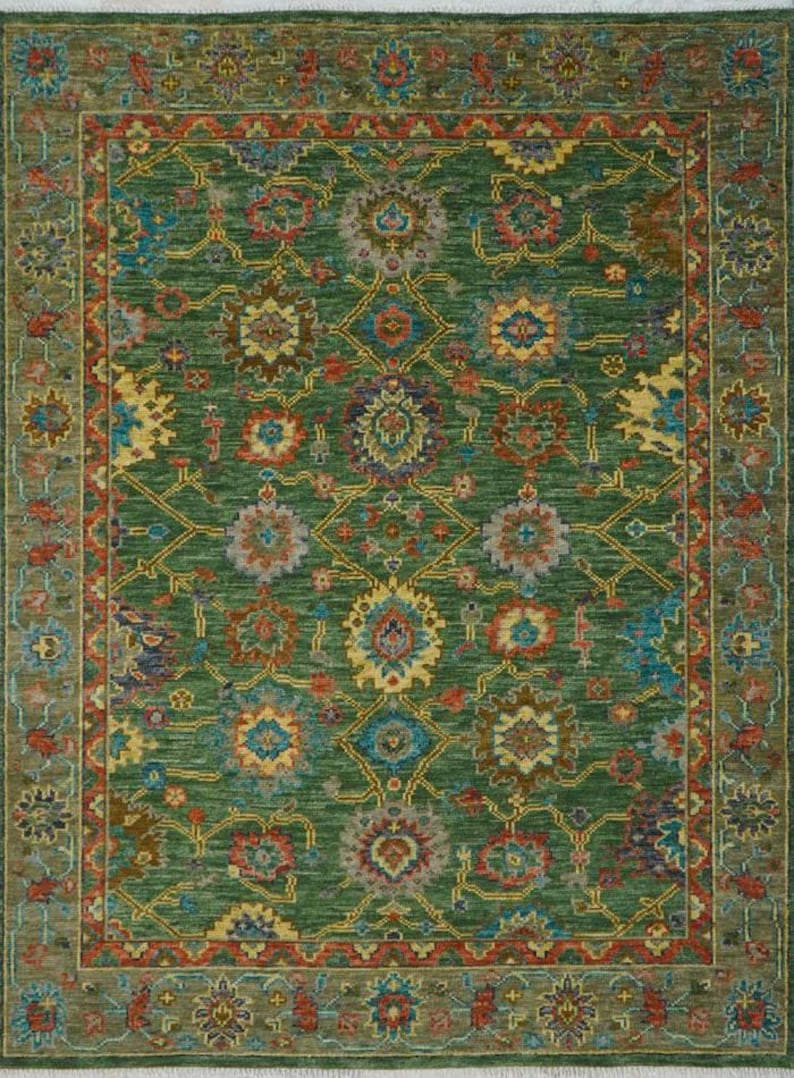 Op de afbeelding: Een rechthoekig groen tapijt met een ingewikkeld bloemmotief in tinten blauw, geel, rood en bruin. Het tapijt heeft een gedetailleerde rand met vergelijkbare kleuren en ontwerpen. Het algehele ontwerp is symmetrisch en sierlijk, voor interieurdecoratie.