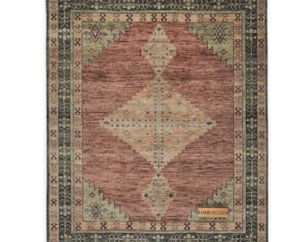 May include: Rectangular area rug with a central diamond pattern in shades of red, beige, and green. The rug has a dark border with repeating geometric designs and the text "HANKWOVEN".