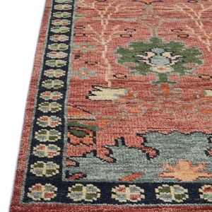 Puede incluir: Una secci&oacute;n de una alfombra estampada en rojo y azul. La alfombra presenta un dise&ntilde;o central con motivos florales verdes, azules y naranjas. Un borde azul oscuro con patrones florales repetidos enmarca el borde. La alfombra tiene una apariencia texturizada.