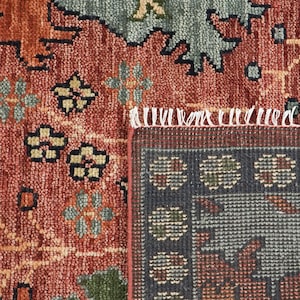 Puede incluir: Primer plano de una secci&oacute;n de una alfombra estampada. La alfombra presenta una mezcla de colores, incluyendo rojo, verde y azul, con dise&ntilde;os florales y geom&eacute;tricos. La alfombra tiene un borde con flecos y un borde detallado.