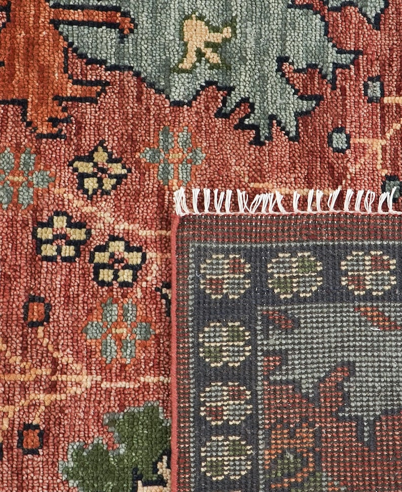 Puede incluir: Primer plano de una secci&oacute;n de una alfombra estampada. La alfombra presenta una mezcla de colores, incluyendo rojo, verde y azul, con dise&ntilde;os florales y geom&eacute;tricos. La alfombra tiene un borde con flecos y un borde detallado.