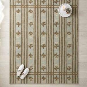 May include: A rectangular area rug featuring a light blue background with vertical brown stripes and a repeating pattern of small, cream-colored acorn motifs. The rug has a structured border design and a textured surface throughout the entire piece.