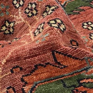 Puede incluir: Primer plano de una alfombra texturizada con un patr&oacute;n detallado. La alfombra presenta una mezcla de colores, incluyendo tonos de rojo, naranja, verde y crema. El dise&ntilde;o incorpora elementos florales y geom&eacute;tricos, creando una apariencia rica y en capas.