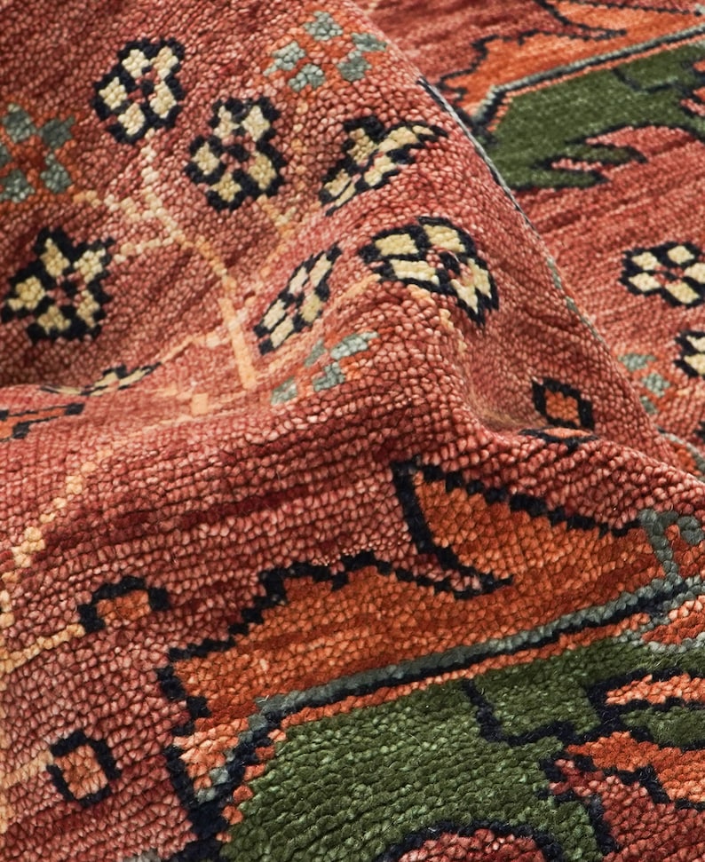 Puede incluir: Primer plano de una alfombra texturizada con un patr&oacute;n detallado. La alfombra presenta una mezcla de colores, incluyendo tonos de rojo, naranja, verde y crema. El dise&ntilde;o incorpora elementos florales y geom&eacute;tricos, creando una apariencia rica y en capas.