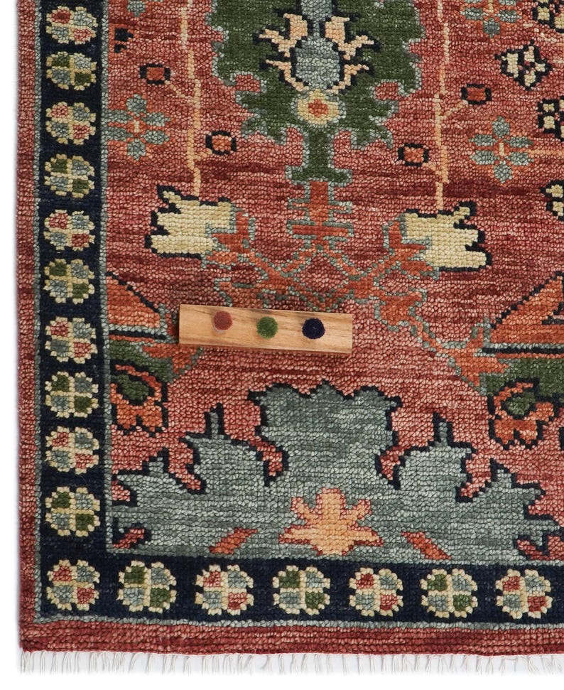Puede incluir: Primer plano de una secci&oacute;n de una alfombra estampada con una muestra de color de madera. La alfombra presenta un fondo rojo con dise&ntilde;os florales verdes, azules y naranjas. Un borde azul oscuro enmarca el borde.