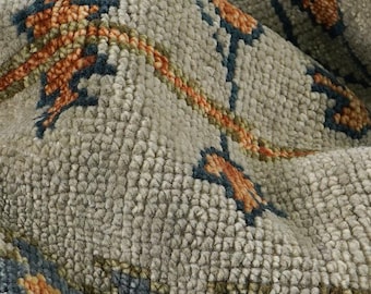 May include: Close-up of a textured rug with a floral pattern. The rug features a light grey background with accents of orange, blue, and green. The design includes stylized floral motifs and a border.
