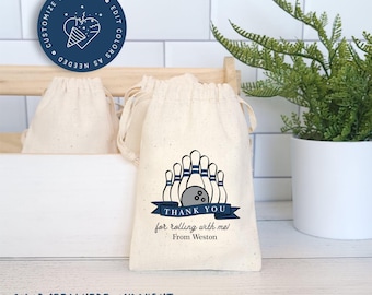May include: A set of white cotton drawstring bags with a blue bowling pin and ball design. The bags have the text "Thank you for rolling with me! From Weston" printed on them.