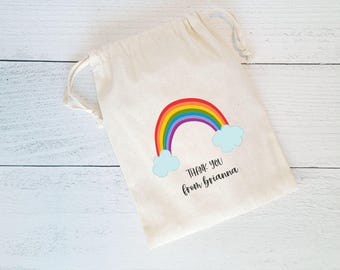 May include: A white cotton drawstring bag with a rainbow and clouds design. The bag has the text "Thank you from Brianna" printed on it.