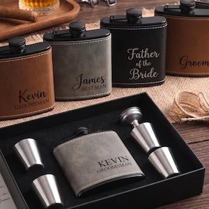 Könnte beinhalten: Eine Sammlung personalisierter Metallflachmänner mit lederartiger Umhüllung in verschiedenen Farben, graviert mit Namen und Titeln wie Kevin Groomsman, James Best Man, Father of the Bride und Groom. Ein Set enthält einen Flachmann und drei Metallbecher.