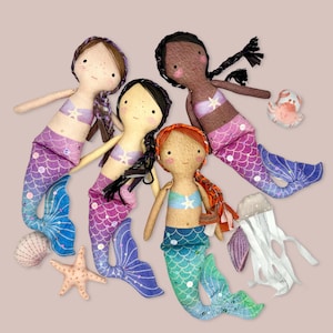 Könnte beinhalten: Vier handgefertigte Meerjungfrauenpuppen mit bunten Stoffschwänzen und Muschelakzenten. Die Puppen haben verschiedene Haarfarben und tragen Muschel-Oberteile.