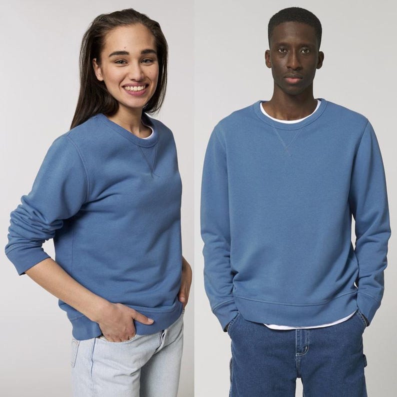 Puede incluir: Dos personas vistiendo sudaderas azules de cuello redondo a juego con camisetas interiores blancas. Las sudaderas tienen un dise&ntilde;o sencillo y la tela parece suave. El fondo es liso, enfatizando la ropa.