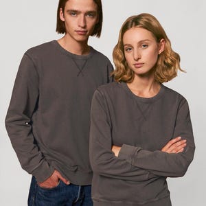 Puede incluir: Dos personas con sudaderas grises antracita con cuello redondo. Las sudaderas tienen un dise&ntilde;o sencillo con un detalle cosido en el cuello. La persona de la izquierda lleva vaqueros azules, mientras que la persona de la derecha tiene los brazos cruzados.