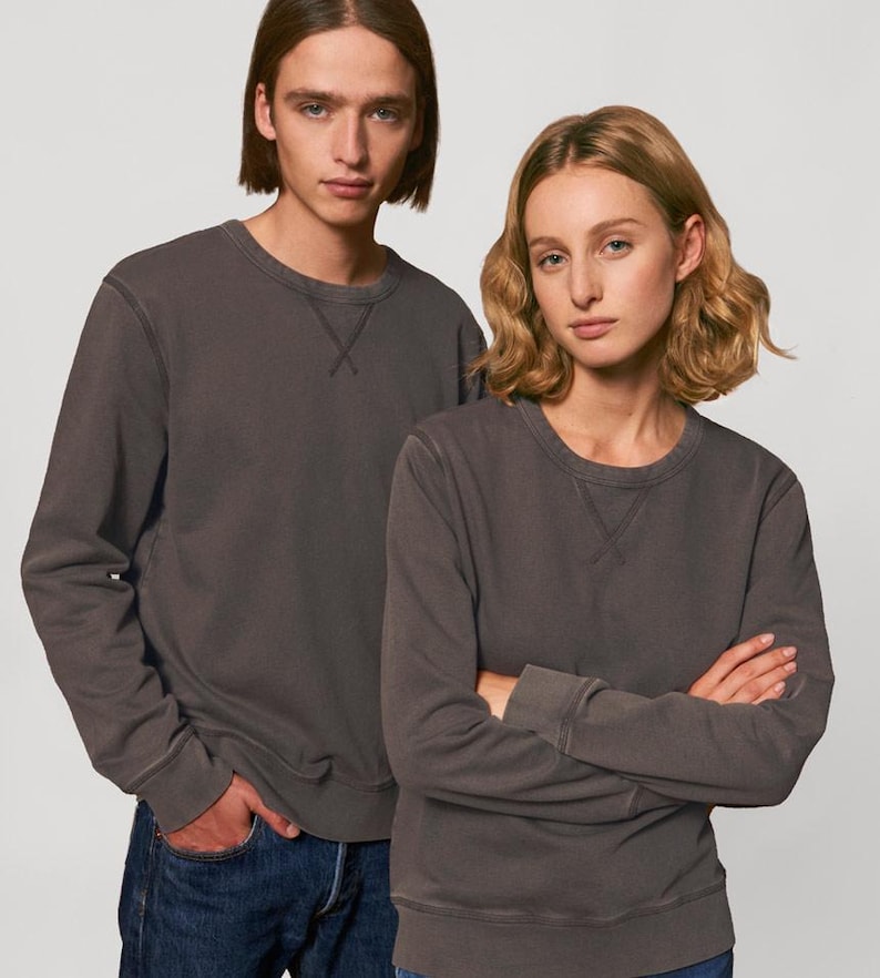 Puede incluir: Dos personas con sudaderas grises antracita con cuello redondo. Las sudaderas tienen un dise&ntilde;o sencillo con un detalle cosido en el cuello. La persona de la izquierda lleva vaqueros azules, mientras que la persona de la derecha tiene los brazos cruzados.
