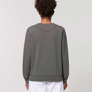 Puede incluir: Una sudadera gris con cuello redondo y mangas largas. La sudadera tiene dobladillo y pu&ntilde;os de canal&eacute;. La modelo lleva pantalones blancos. La espalda de la persona est&aacute; mirando a la c&aacute;mara.