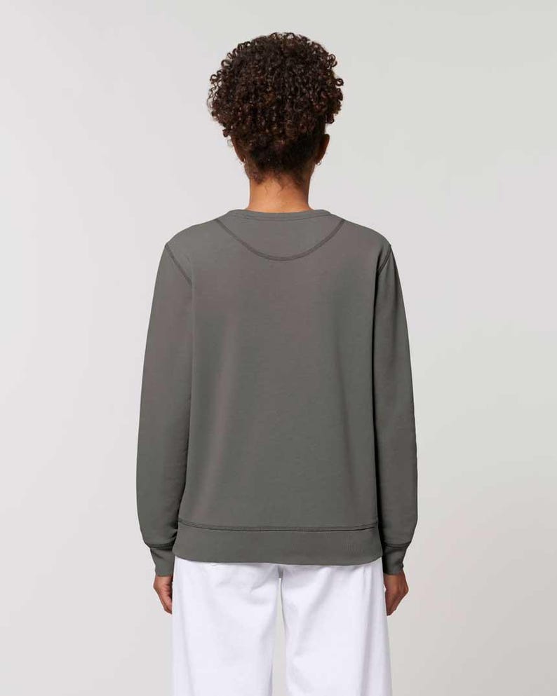 Puede incluir: Una sudadera gris con cuello redondo y mangas largas. La sudadera tiene dobladillo y pu&ntilde;os de canal&eacute;. La modelo lleva pantalones blancos. La espalda de la persona est&aacute; mirando a la c&aacute;mara.
