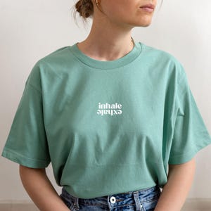 Könnte beinhalten: Ein hellgrünes T-Shirt mit dem Aufdruck "inhale exhale" in Weiß auf der Vorderseite.