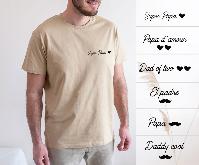 May include: A tan crew neck t-shirt with the text "Super Papa" and a small black heart. Additional text options include "Papa d'amour", "Dad of two", "El padre", "Papa", and "Daddy cool".