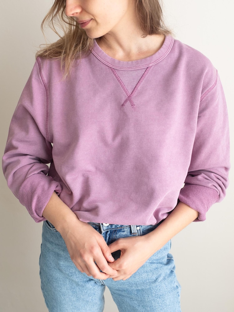May include: A soft, light purple sweatshirt with a crew neck and long sleeves. The sweatshirt has a subtle vintage wash and a relaxed fit.