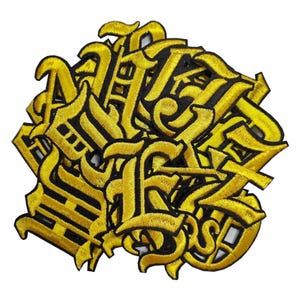 May include: A collection of embroidered patches featuring individual letters of the alphabet in a bold, gold-coloured gothic font with a black border. Each patch is crafted with dense yellow thread, creating a textured, raised appearance for each character.