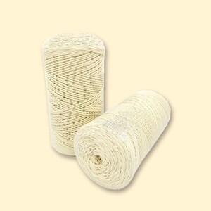 May include: Two cylindrical spools of off-white cotton twine. One spool stands vertically while the other rests horizontally in front, showcasing the tightly wound, multi-ply cord structure and the textured surface of the natural fiber string.