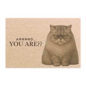 Puede incluir: Felpudo rectangular con un gato gris de aspecto gruñón y ojos verdes. El texto "ANNNND... YOU ARE??" está impreso en negro sobre un fondo marrón claro. El gato tiene una expresión severa.