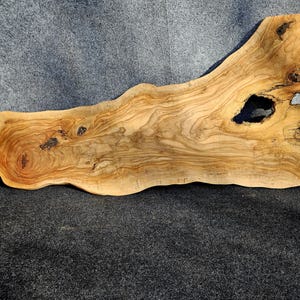 Può includere: Una grande lastra di legno naturale con una forma irregolare unica e un nodo. Il legno ha un colore ricco e marrone con una bella venatura.