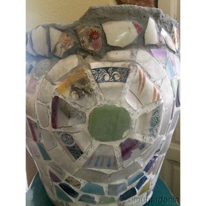 May include: A large, round planter made of concrete and decorated with a mosaic of broken china. The mosaic features a variety of colors, including white, blue, green, red, and purple.