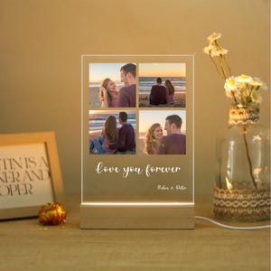 Könnte beinhalten: Eine personalisierte Fotoanzeige mit vier Bildern von Paaren am Strand, beleuchtet von einer LED-Leuchte. Die Worte "love you forever" sind auf der Vorderseite geschrieben, mit Namen darunter. Der Sockel ist aus Holz.