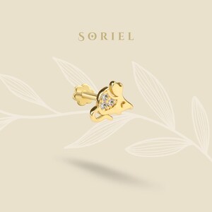 May include: A gold-colored stud earring in the shape of a mouse, with three small, clear gemstones set in the mouse's body. The earring has a post and a flower-shaped backing. The brand name "SORIEL" is displayed above the earring.