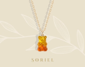 Könnte beinhalten: Eine goldfarbene Halskette mit einem Gummibären-Anhänger. Der Gummibär hat einen Farbverlauf von Gelb zu Orange. Die Kette hat ein filigranes Kettenglied-Design. Das Wort "SORIEL" ist unten im Bild aufgedruckt.