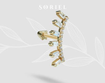 May include: A gold-colored ear cuff featuring a star-shaped post and a curved design. The cuff is adorned with rectangular and round clear gemstones. The word "SORIEL" is printed at the top.