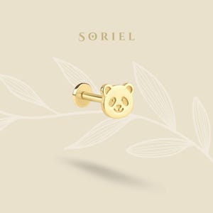 May include: A gold-colored stud earring featuring a panda bear design. The panda's face is detailed with etched eyes, nose, and a smiling mouth. The earring has a flat back and a post for piercing. The brand name "SORIEL" is displayed at the top.